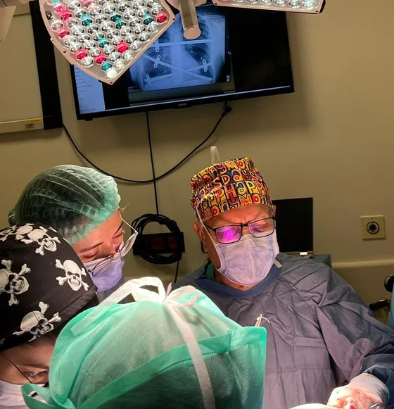 Prof. Dr. Mustafa Yüksel operating, with a chest X-ray showing implanted pectus correction bars on the monitor behind him